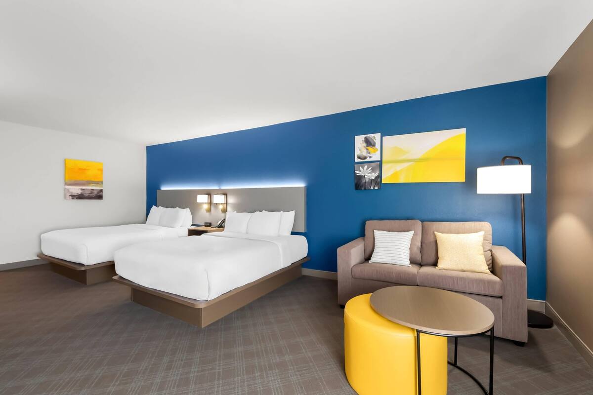 A hotel room with a bed, a sofa, a small table, and a lamp.