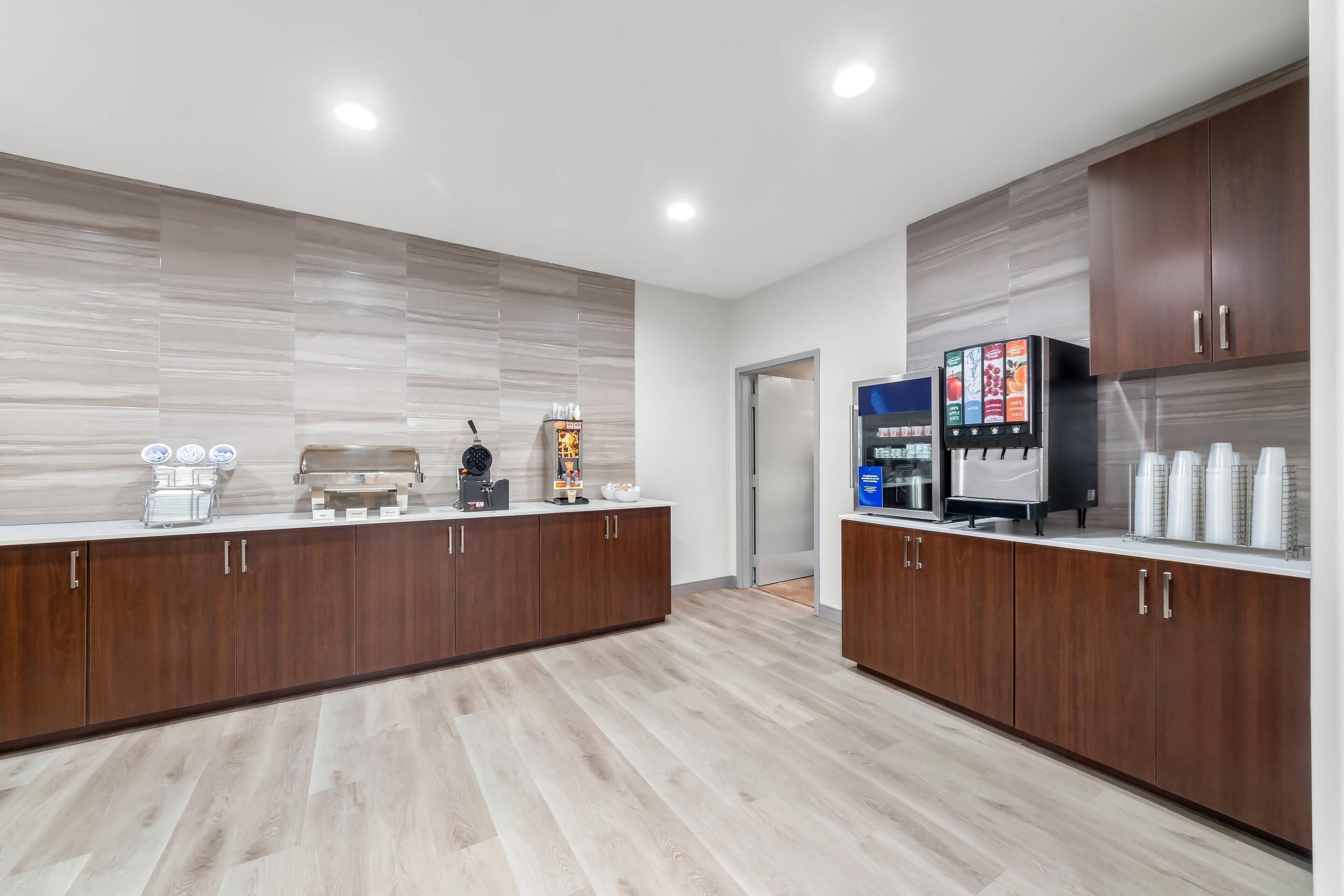 A modern kitchen with wooden cabinets, a coffee machine, a tea station, and a refrigerator with a digital display.