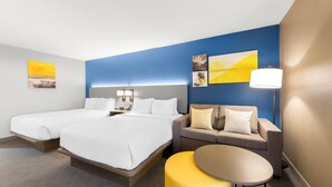 Une chambre d’hôtel avec deux lits, un canapé, une petite table et des œuvres d’art accrochées aux murs.