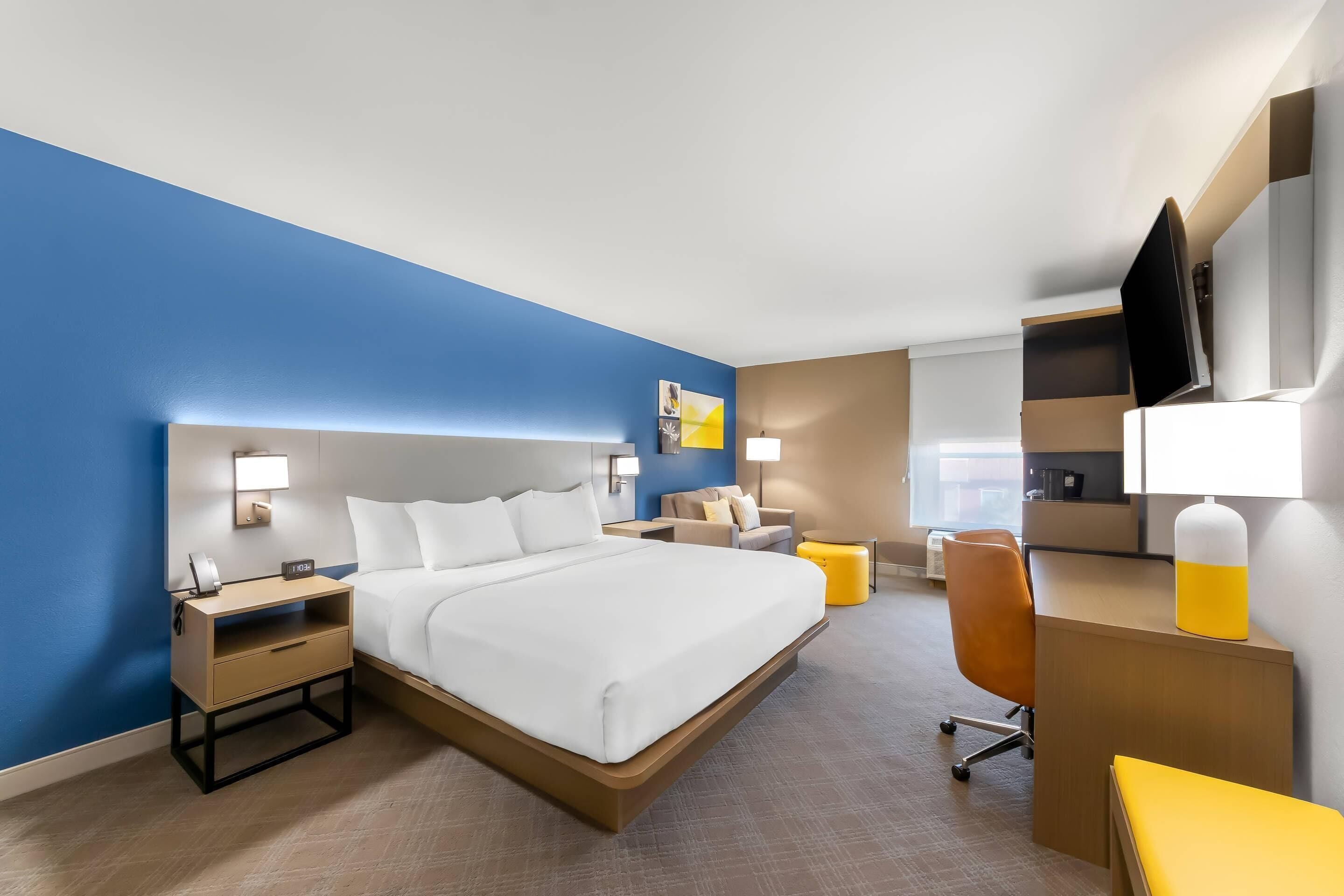 A modern hotel room with a large bed, bedside tables, a desk, a chair, and a TV.