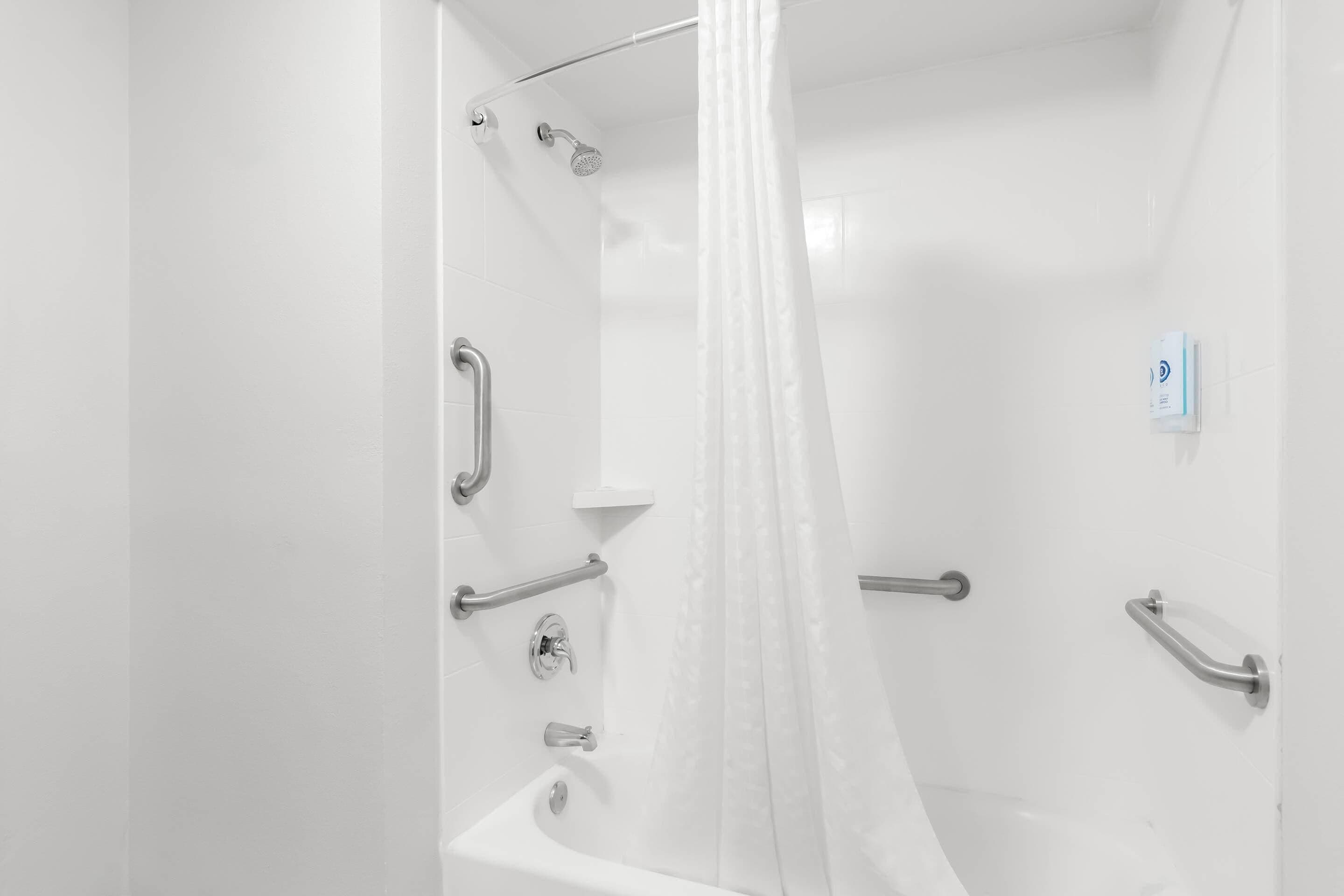 A modern bathroom with a bathtub, shower, and handrails.