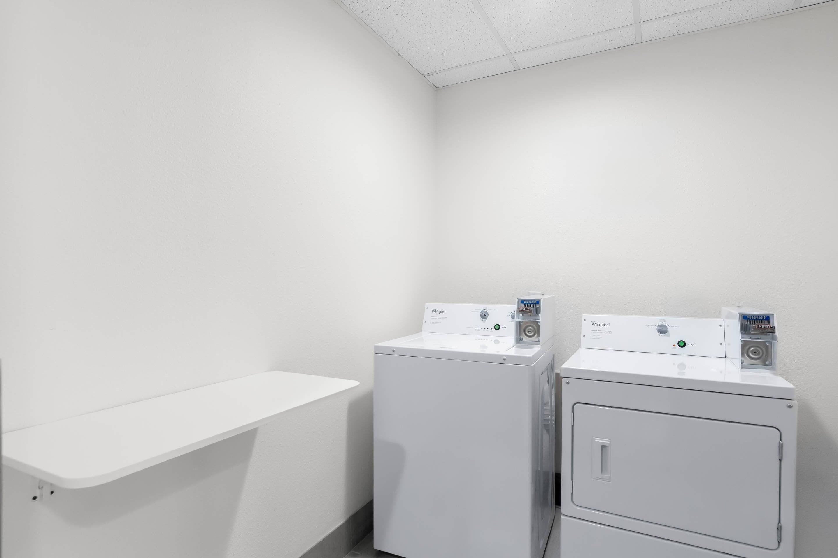 A laundry room with two white Whirlpool washers and a white shelf.