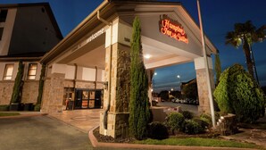 A hotel entrance with a stone facade, a neon sign, and a clear sky.