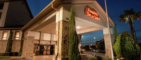 A hotel entrance with a stone facade, a neon sign, and a clear sky.