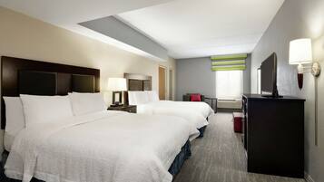 A hotel room with two beds, a desk, a chair, a TV, and a lamp.