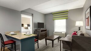 A compact hotel room with a kitchenette, a dining area, a sofa, and a TV.
