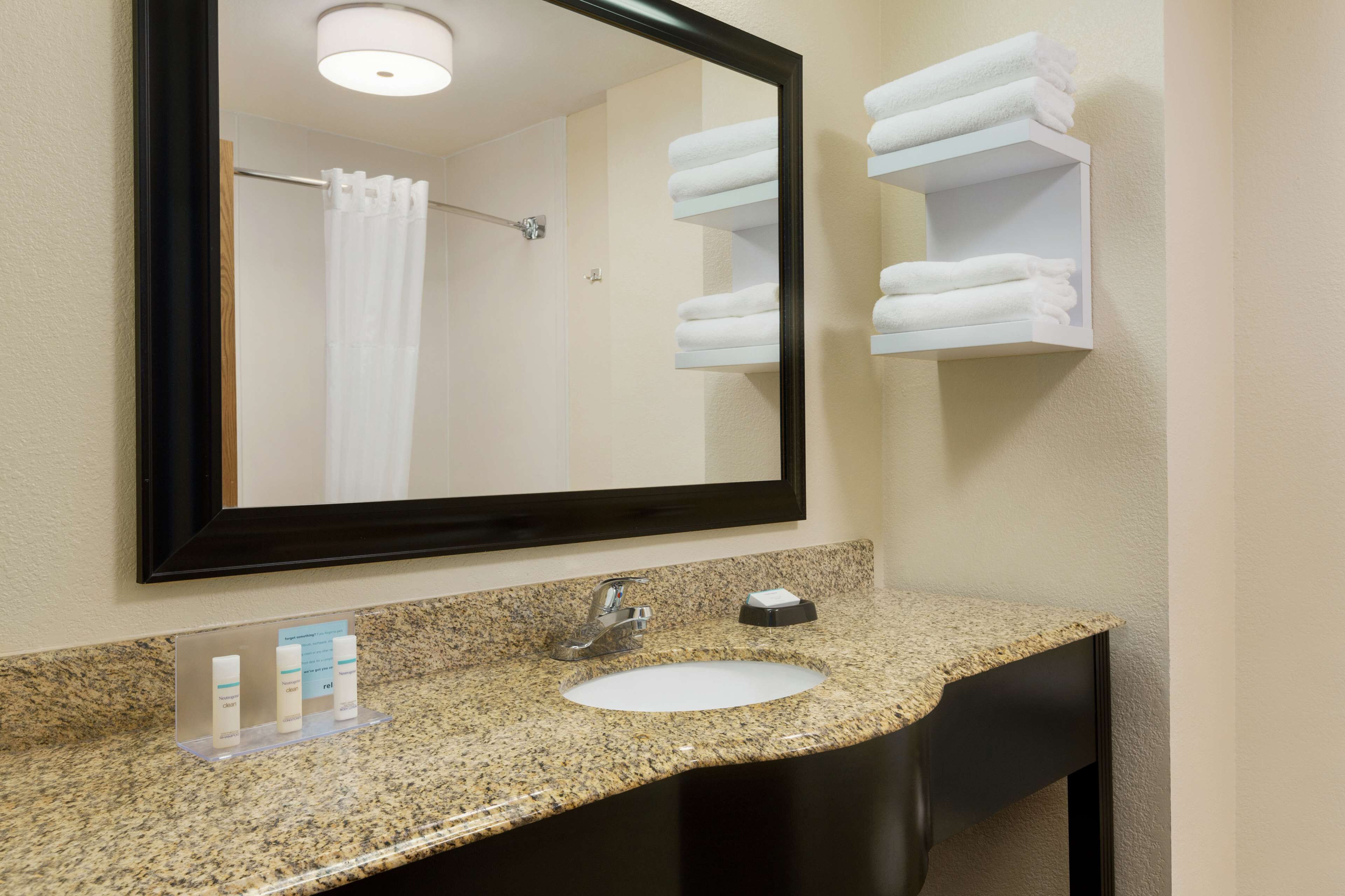A bathroom with a granite countertop, a white sink, a mirror, and a towel rack with folded towels.