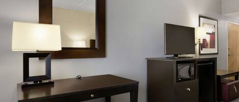 A hotel room with a desk, a chair, a television, a microwave, and a cabinet.