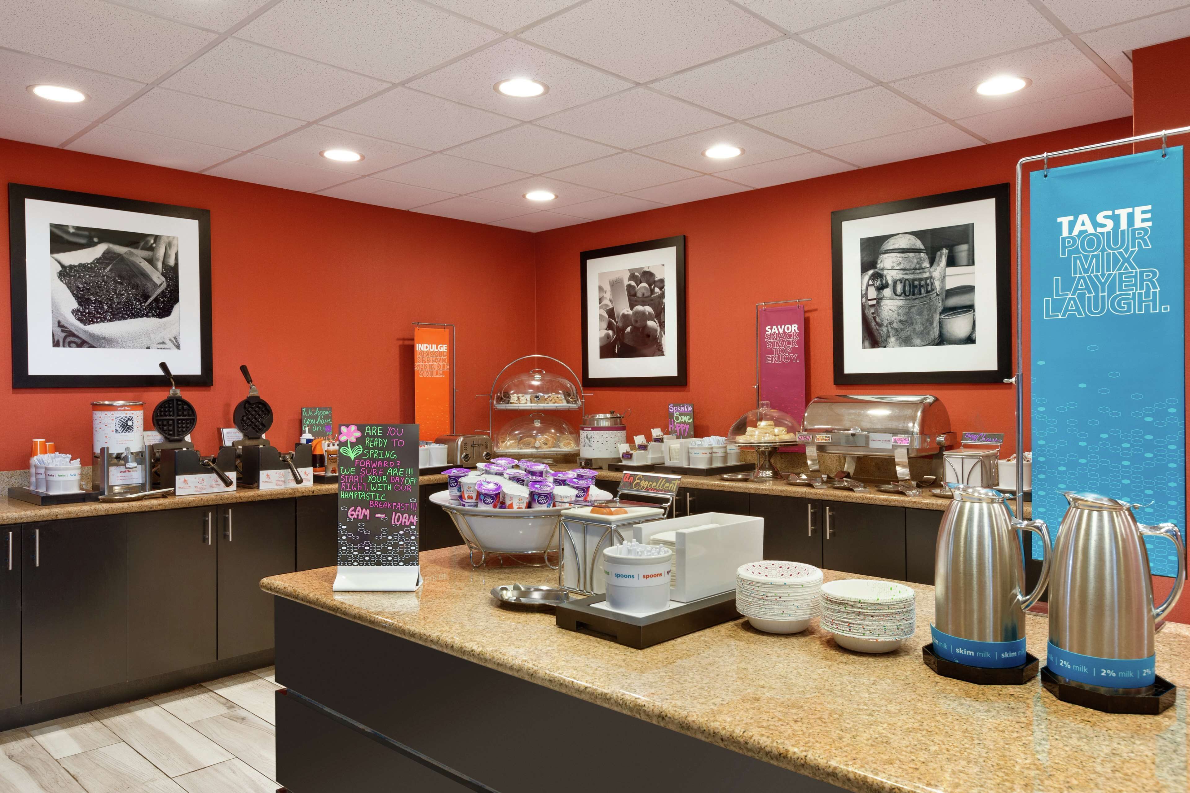 Un buffet de petit-déjeuner proposant une variété d’aliments, des machines à café et un panneau sur lequel on peut lire : « GOÛTEZ, PARTAGEZ, RIEZ. »