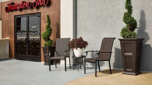 A Hampton Inn exterior with a wooden facade, two potted plants, and a seating area with wicker chairs and a table. - Hampton Inn Massillon (Massillon)