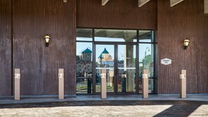 A hotel entrance with a large glass door, wooden walls, and two wall-mounted light fixtures. - Hampton Inn Massillon (Massillon)