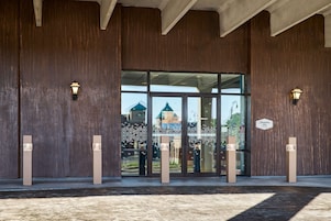 Entrada de hotel con una puerta de cristal grande, paredes de madera y dos lámparas fijadas a la pared.