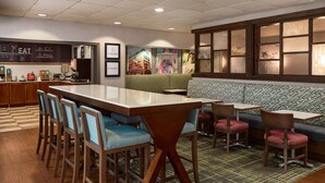 A restaurant with a long counter, bar stools, a booth, and a patterned carpet. - Hampton Inn Massillon (Massillon)