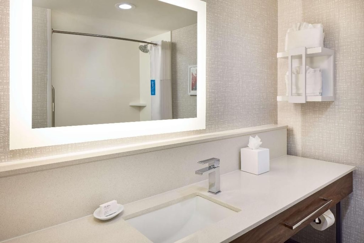 A bathroom with a large mirror, a sink, a towel rack, and a shower area.