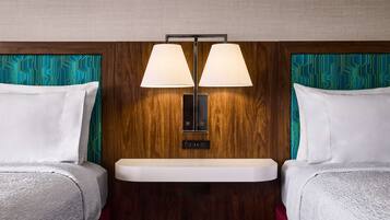 Habitación de hotel con dos camas, cabecero de madera, mesita de noche y lámpara de pared.