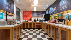 Une cuisine moderne avec un carrelage à motifs, des meubles en bois et un comptoir où sont exposés divers appareils et produits alimentaires.