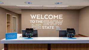 Un comptoir d’accueil d’hôtel avec une pancarte indiquant « Bienvenue dans le Missouri », deux lecteurs de cartes et une pancarte « Hilton Honors ».