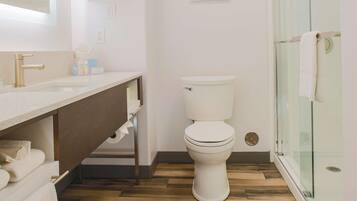 A modern bathroom with a wooden floor, white fixtures, and a glass shower enclosure.