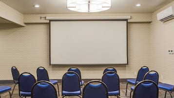 Un salón de conferencias con una pantalla grande, sillas azules y un candelabro.