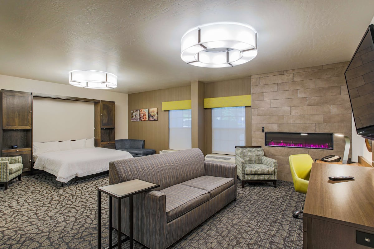 A hotel room with a bed, a sofa, a desk, a chair, and a fireplace.