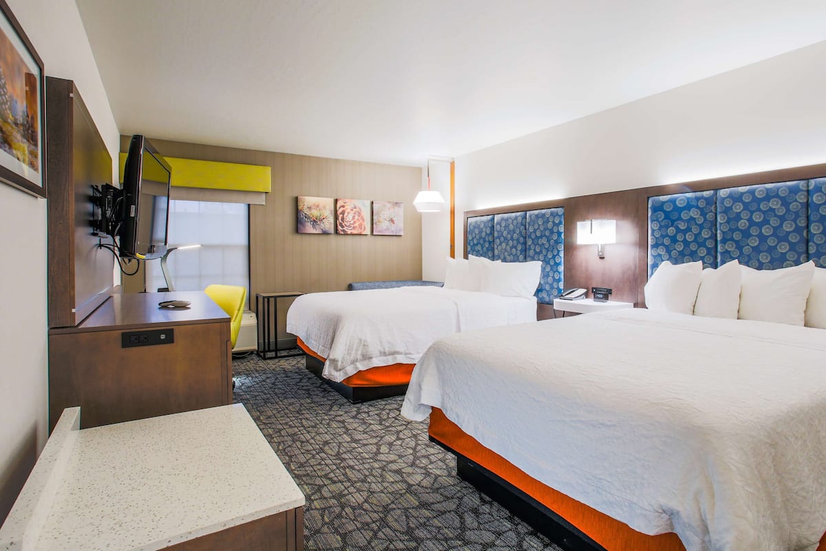 A hotel room with two beds, a desk with a computer, a chair, and a small table.