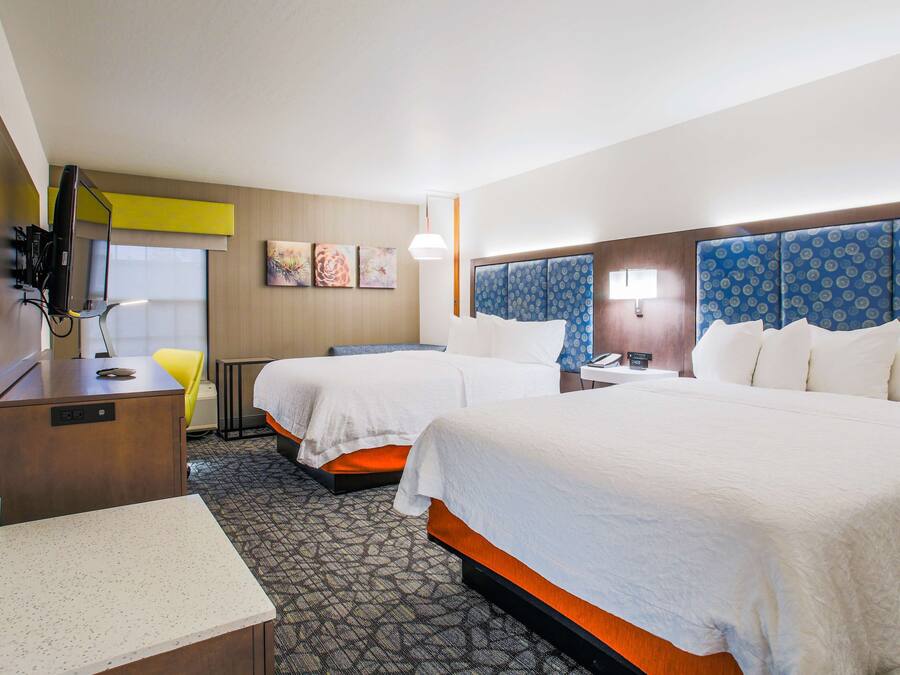 A hotel room with two beds, a desk with a computer, a chair, and a small table.