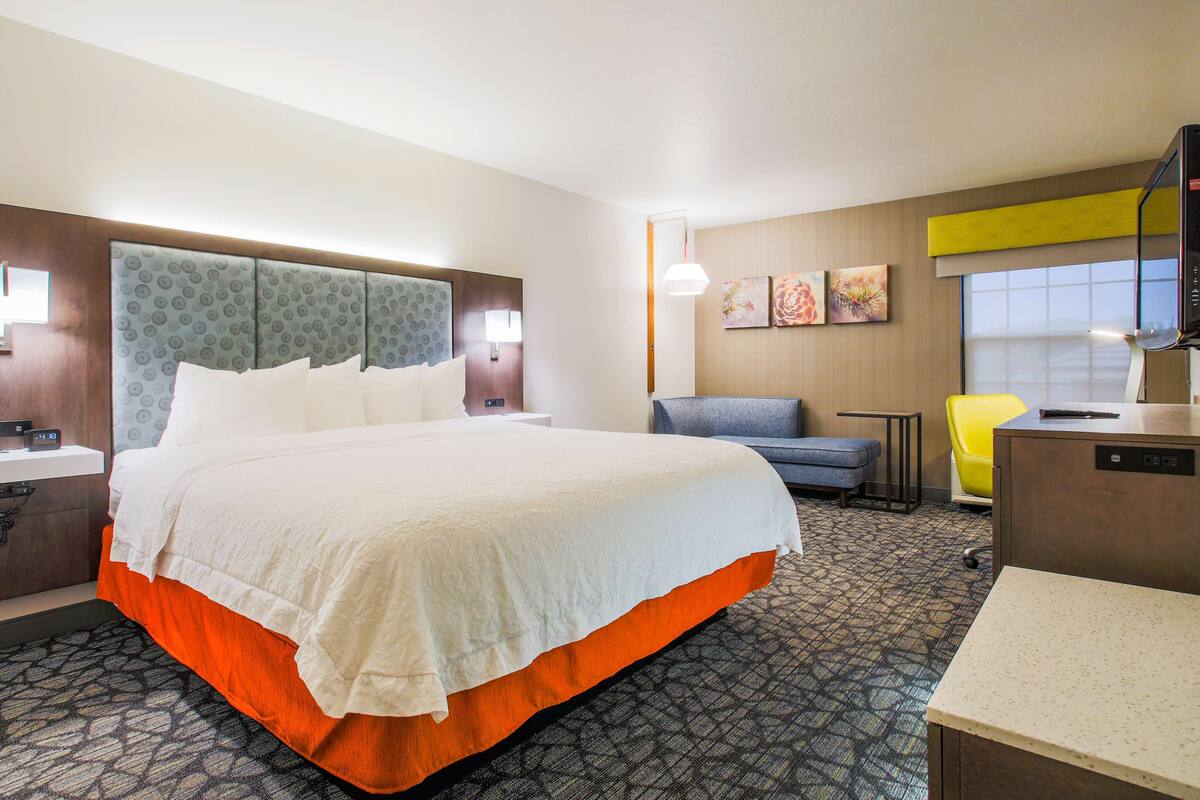 A hotel room with a large bed, a desk with a chair, a television, and artwork on the wall.
