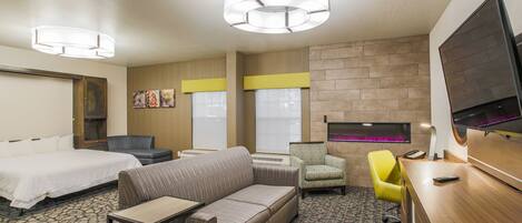 A hotel room with a bed, a sofa, a desk, a chair, and a television.
