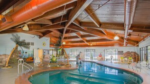 An indoor swimming pool with a wooden ceiling, a palm tree, and a mural on the wall.