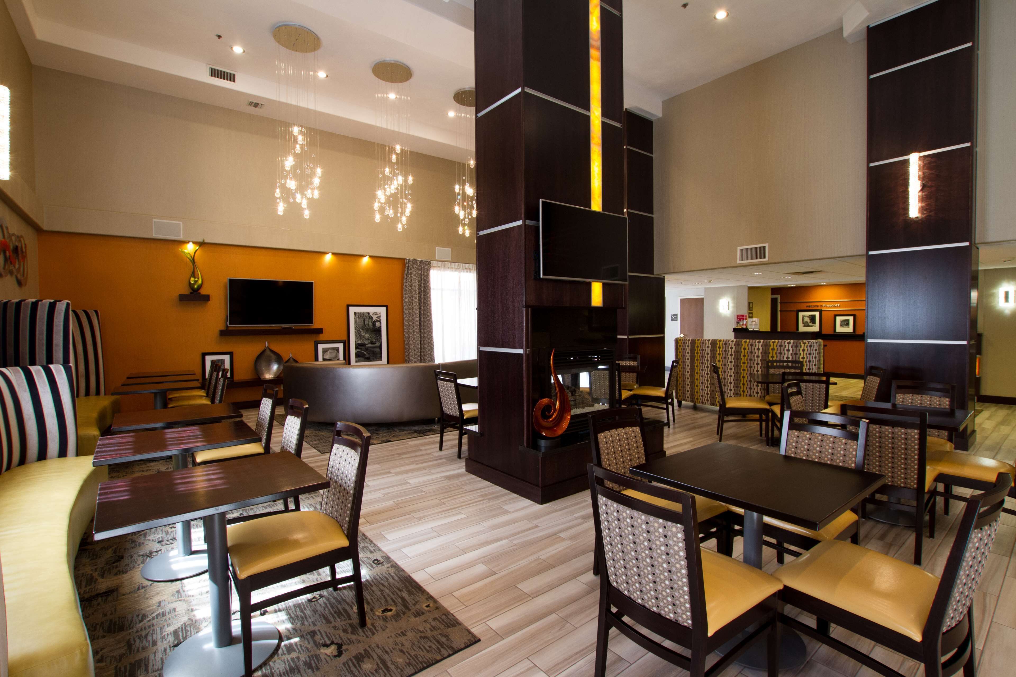 A modern restaurant with high tables and booths, a fireplace, and a TV mounted on the wall.