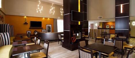 A modern restaurant with high tables and booths, a fireplace, and a TV mounted on the wall.