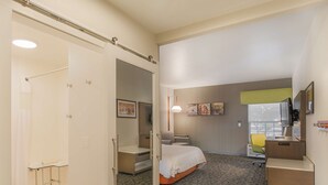 A hotel room with a bed, a desk, a chair, a mirror, and artwork on the wall.