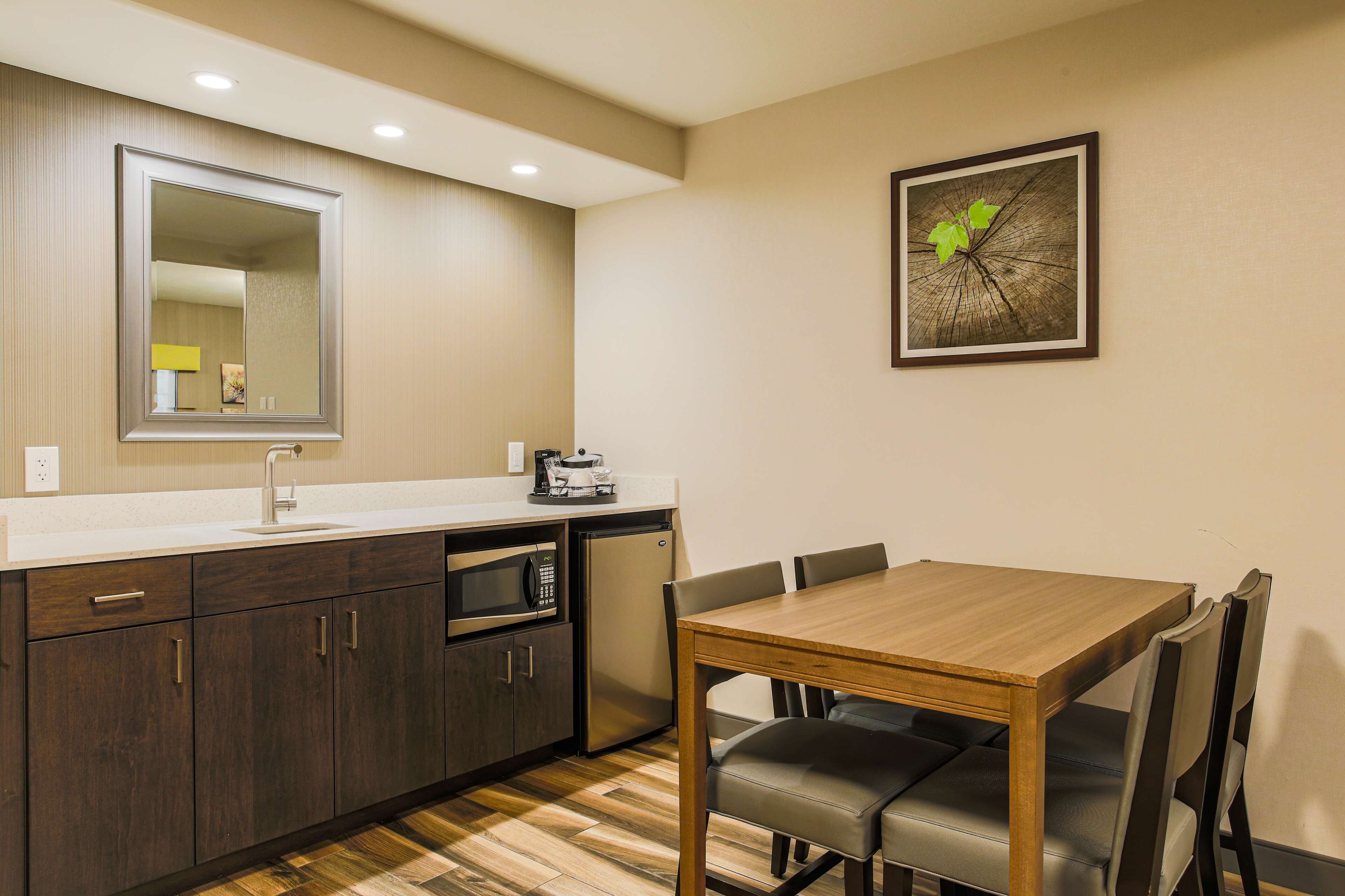 A compact kitchen with a microwave, sink, and small refrigerator. There is a wooden dining table with four chairs.