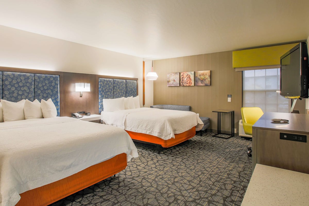 A hotel room with two beds, a desk, a chair, and a television.