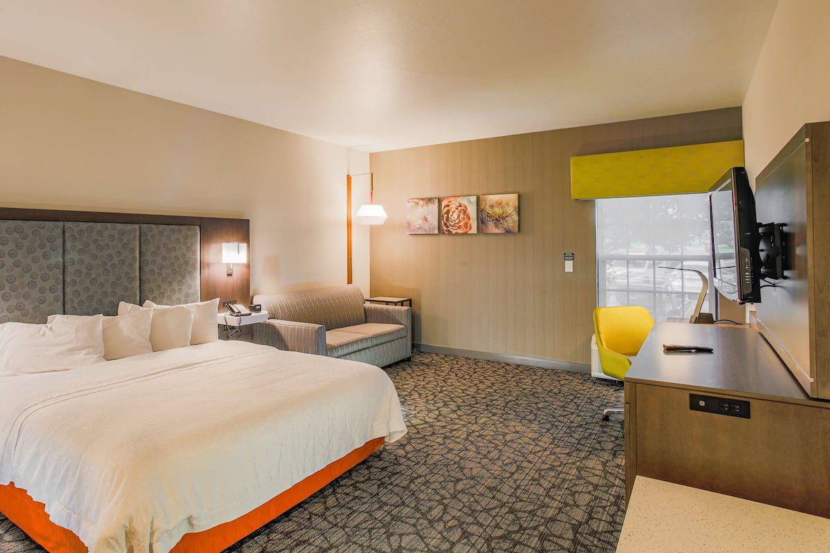A hotel room with a large bed, a desk with a computer, a chair, and a TV.