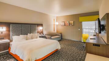A hotel room with a large bed, a desk with a computer, a chair, and a TV.
