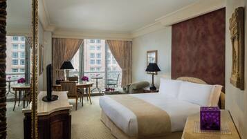 Une chambre d’hôtel avec un grand lit, un bureau, une chaise, une table ornée de fleurs et une vue sur les bâtiments par la fenêtre.