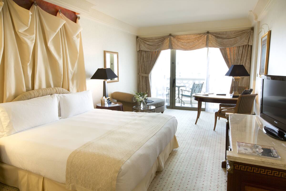 Une chambre d’hôtel avec un grand lit, deux tables de chevet, une télévision et un balcon équipé d’une table et de chaises.