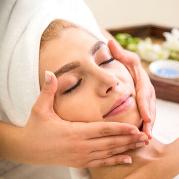 A person receiving a facial treatment with a tray of flowers and bowls of products.