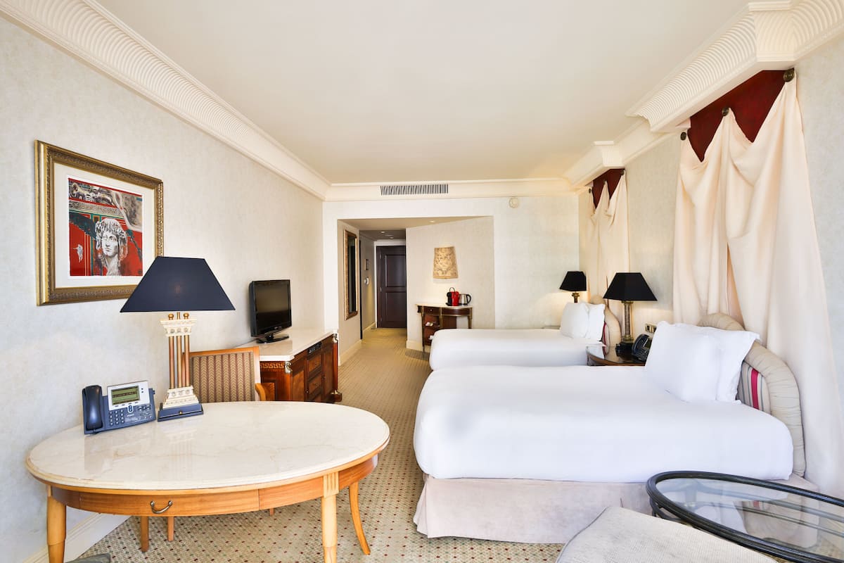 Une chambre d’hôtel comprenant un lit, deux tables de chevet, un bureau, une chaise, un téléviseur et un téléphone.