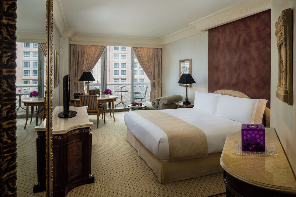 Une chambre d’hôtel avec un grand lit, un bureau, une chaise, une petite table et une vue sur la ville grâce à de grandes fenêtres.