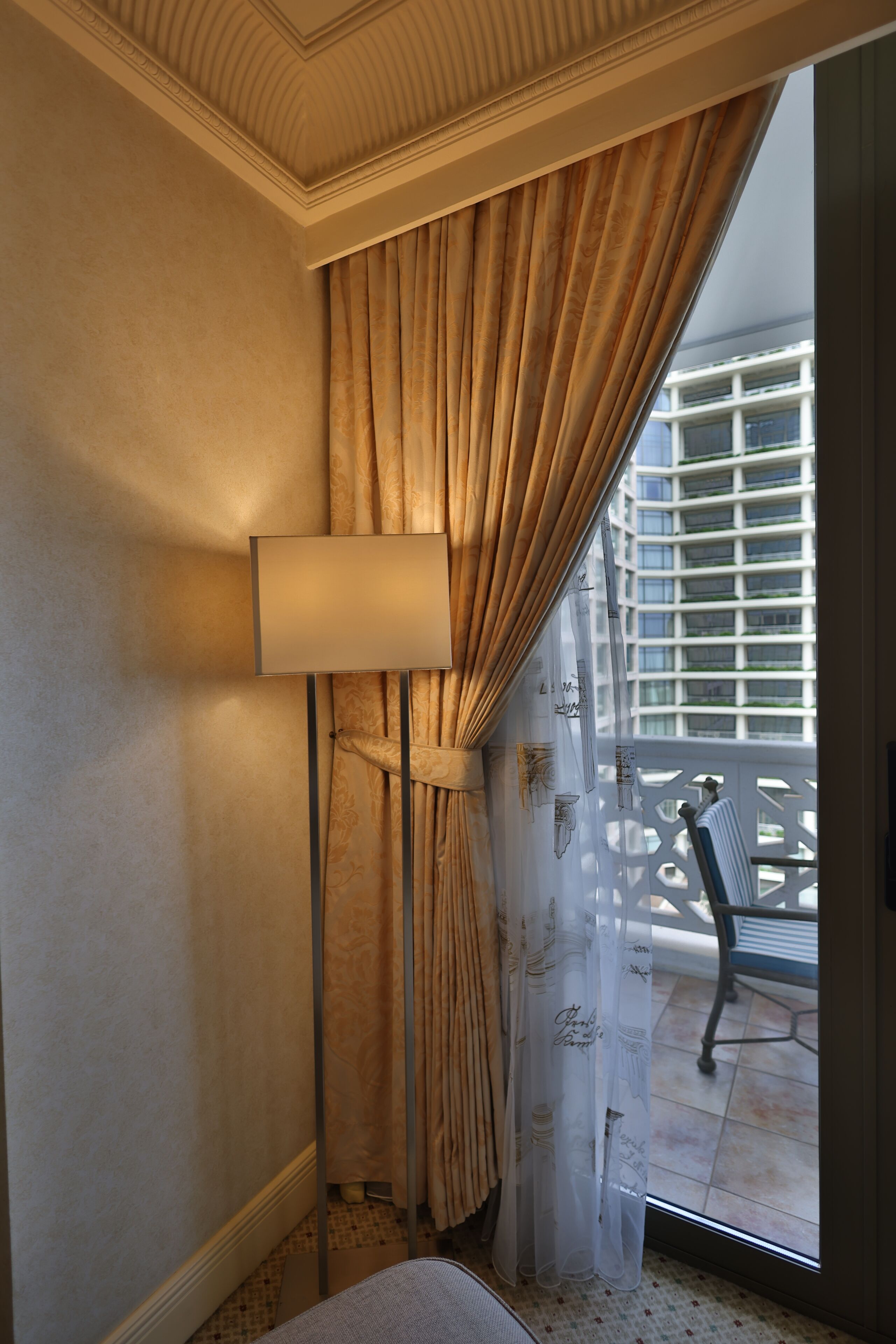 Una habitación con un ventanal grande, una lámpara de pie y vistas a un edificio.