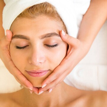 A person receiving a facial treatment with a tray of essential oils and herbs nearby.