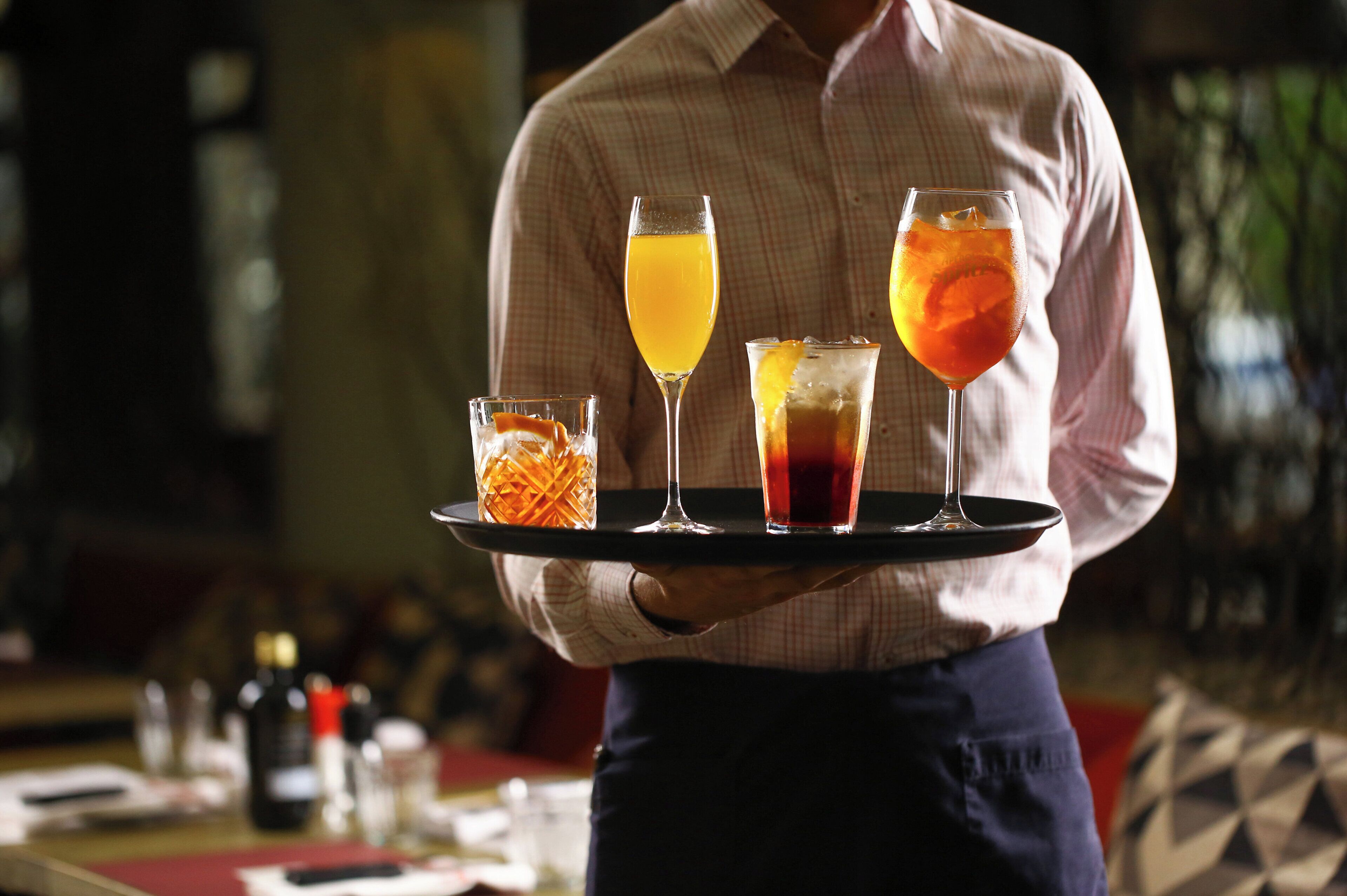 Una persona sosteniendo una bandeja con cuatro vasos de diferentes bebidas.