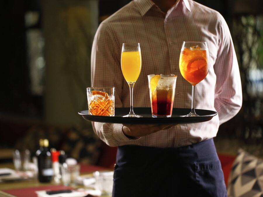 Una persona sosteniendo una bandeja con cuatro vasos de diferentes bebidas.