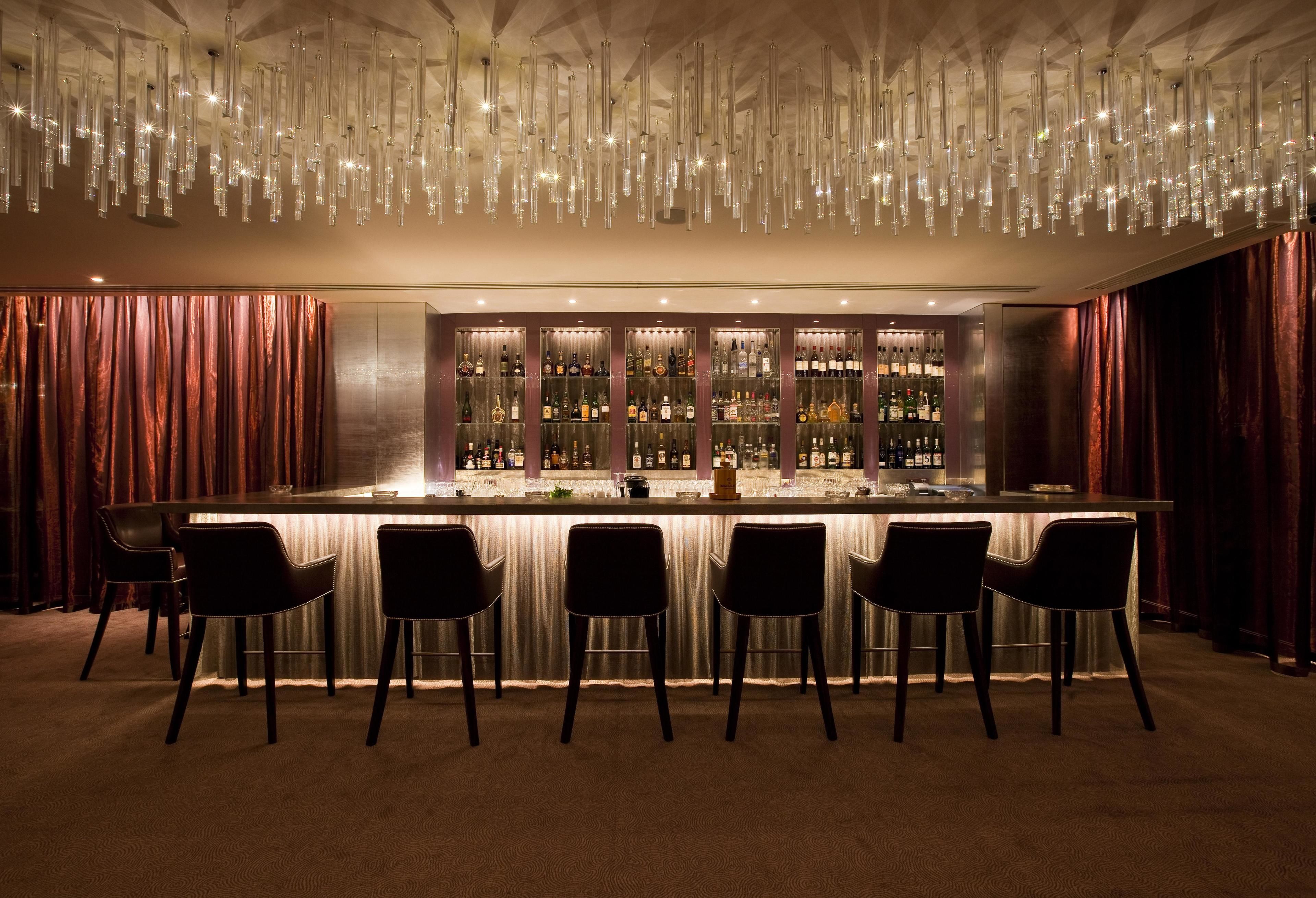 A bar area with a long counter, multiple bar stools, and a well-stocked bar.