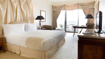 Habitación de hotel con una cama grande, un escritorio con silla, televisor y balcón con cortinas.