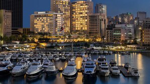 Puerto deportivo con numerosos yates amarrados, rodeado de edificios altos cuyas ventanas iluminadas reflejan un paisaje urbano.