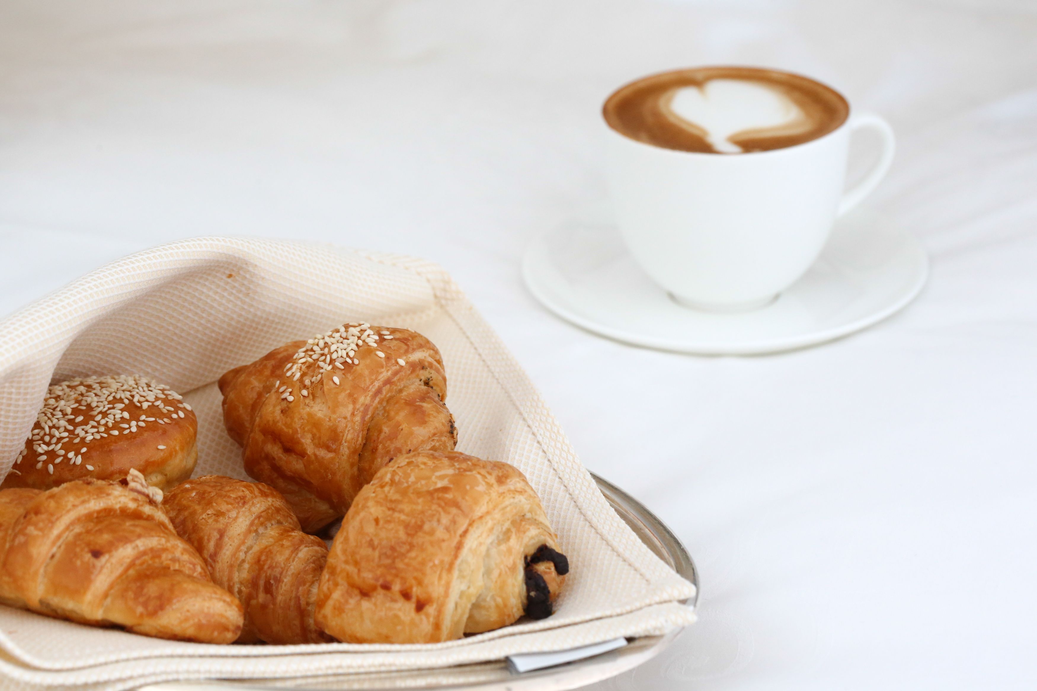 A tray of croissants and a cup of coffee on a white table.