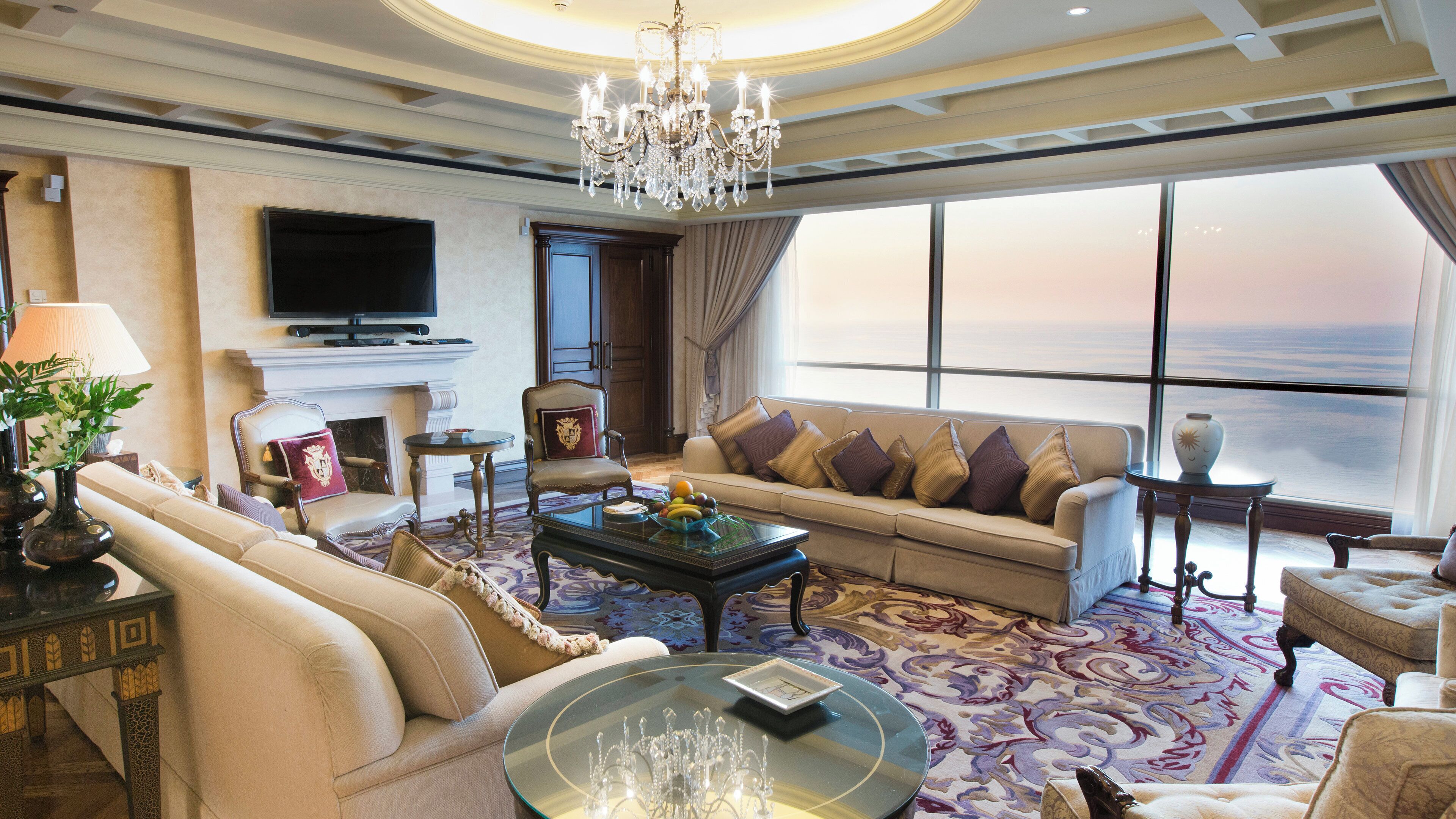 A luxurious living room with a chandelier, sofas, a television, and a large window with a view.